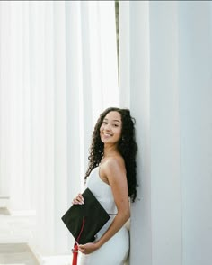 a woman in a white dress leaning against a column holding a black purse and smiling