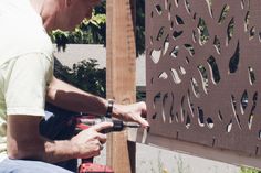 a man is working on a piece of metal art in his backyard with a power drill