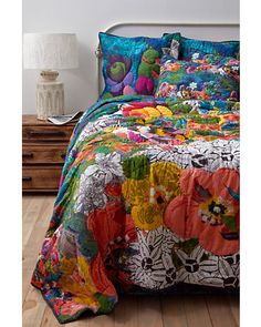 a bed covered in lots of colorful flowers on top of a wooden floor next to a night stand