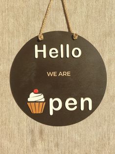 a sign that says, hello we are open with a cupcake hanging from it