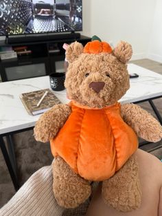 a brown teddy bear wearing an orange shirt sitting on someone's lap in front of a television