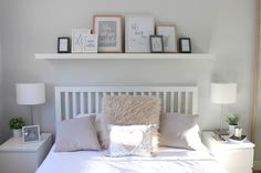 a white bed topped with pillows next to two framed pictures on top of the headboard