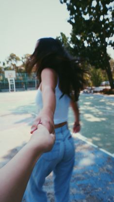 a person holding the hand of another person on a skateboard near a basketball court