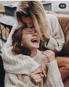 two women are laughing together while sitting on a couch with their arms around each other