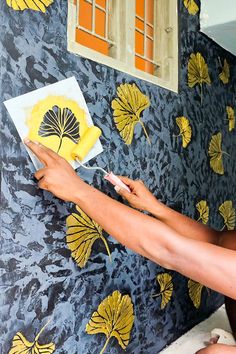 a woman is painting on a wall with yellow flowers