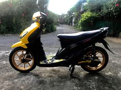 a yellow and black scooter parked on the side of a road next to bushes