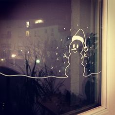 a window with a drawing of a snowman on it's glass and the reflection of buildings in the window