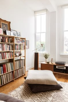 a living room filled with lots of books on top of a hard wood floor next to a window