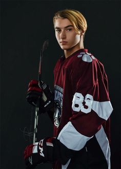 a young man holding a hockey stick and wearing a maroon jersey with the number 86 on it