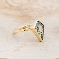 a gold ring with a green and white stone in the center on a wooden surface