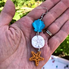 a person is holding two charms in their hand, one has a starfish and the other has a seashell