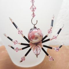 a pink and black beaded spider ornament hanging from a white glass ball