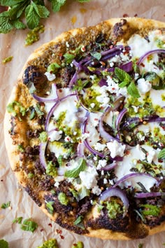 a pizza topped with onions, cheese and green herbs on top of parchmented paper