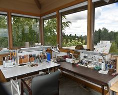 a desk with many pens and pencils on it in front of large windows overlooking trees