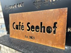 a metal sign that says cafe seelohf on the side of a bench in front of a brick wall