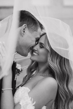 black and white photo of bride and groom embracing each other with veil blowing in the wind