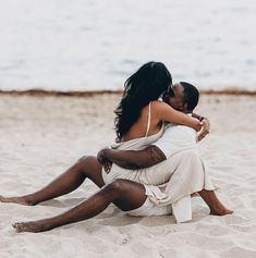 a man and woman sitting on the beach hugging