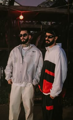 two men standing next to each other in front of a building with lights on it