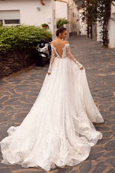 a woman in a wedding dress standing on a cobblestone road with her back to the camera