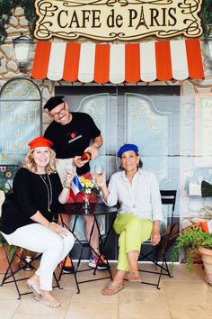 three people are sitting at a table in front of a cafe