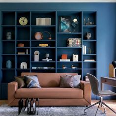 a living room filled with furniture and bookshelves next to a desk in front of a blue wall