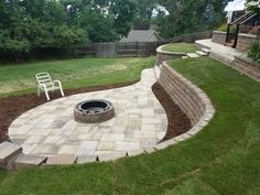 a fire pit in the middle of a yard with steps leading up to it and a white chair next to it