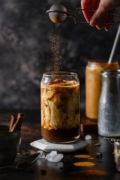 someone is sprinkling cinnamon into a jar filled with coffee and ice cubes