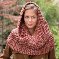 a woman wearing a knitted scarf with a hood on her head, in front of some trees