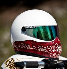 a white helmet with green and red designs on it's face is sitting on the back of a motorcycle