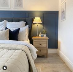 a bed with white and black pillows in a bedroom next to a night stand, lamp and pictures on the wall