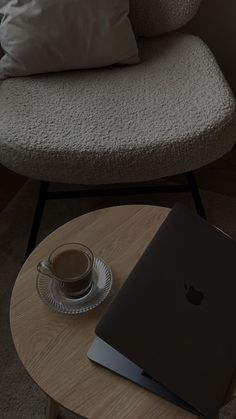 an apple laptop sitting on top of a wooden table next to a cup of coffee