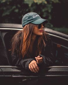 a woman in sunglasses and a hat leaning out the window of a car