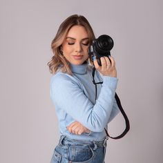 a woman holding a camera up to her face and looking at the camera with both hands