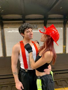 a man and woman standing next to each other in front of a train station platform