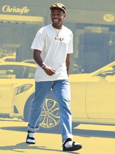 a man walking across a parking lot next to a yellow car