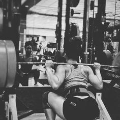 a man squats in front of a barbell while holding a weight machine behind his back