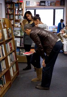 several people standing in a library looking at books on shelves and one person leaning over the book shelf