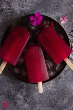 three popsicles are sitting on a plate with purple flowers in the middle and pink petals around them