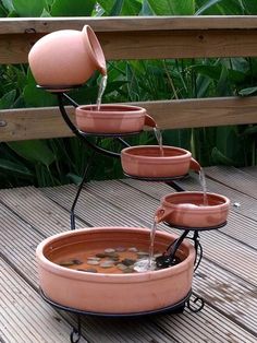 three planters with water pouring from them on a wooden deck in front of green plants