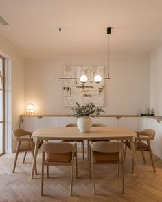 a dining room table with four chairs and a vase on the table in front of it