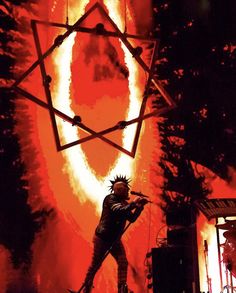 a man standing on stage in front of a giant orange and black star with flames coming out of it