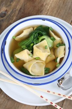 a white bowl filled with dumplings and broccoli on top of a wooden table