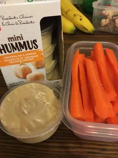 carrots, yogurt and bananas sitting on a table next to a box of hummus