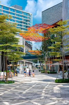 people are walking down the sidewalk in front of tall buildings with trees on each side