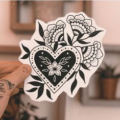 a person holding up a sticker with a heart and flower design on it's side