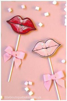 two candy lollipops with pink bows and lipstick on them are laying next to marshmallows