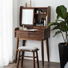 a wooden vanity with mirror and stool next to a potted plant on the floor