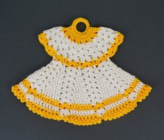 a crocheted yellow and white dress hanging from a hook on a gray surface