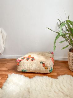 a plant in a pot next to a footstool and rug on the floor