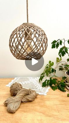 a woven ball hanging from a rope on top of a wooden table next to a potted plant